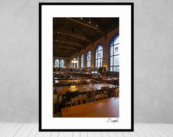 May include: A large, well-lit library with rows of wooden tables and chairs. The room has high ceilings with exposed wooden beams and large windows. The windows are framed with stone and have a view of the outside.