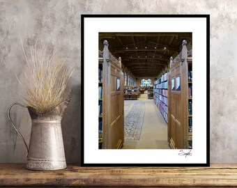 May include: A framed photograph of a library interior with wooden bookshelves and a long hallway lined with books. The hallway is carpeted and has a wooden ceiling with exposed beams.