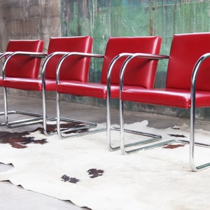 May include: Four red leather chairs with chrome frames. The chairs are arranged in a row on a white and brown cowhide rug.