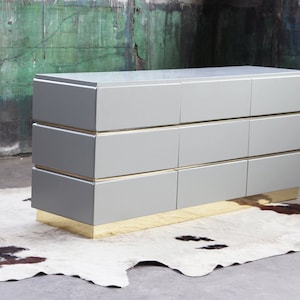 May include: A gray dresser with eight drawers and a brass base. The dresser has a sleek, modern design and is made of high-quality materials.