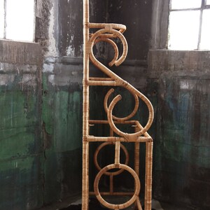 May include: A tall, natural woven rattan shelf unit with a unique, curved design. The shelf has four levels and is made of natural, light brown rattan.