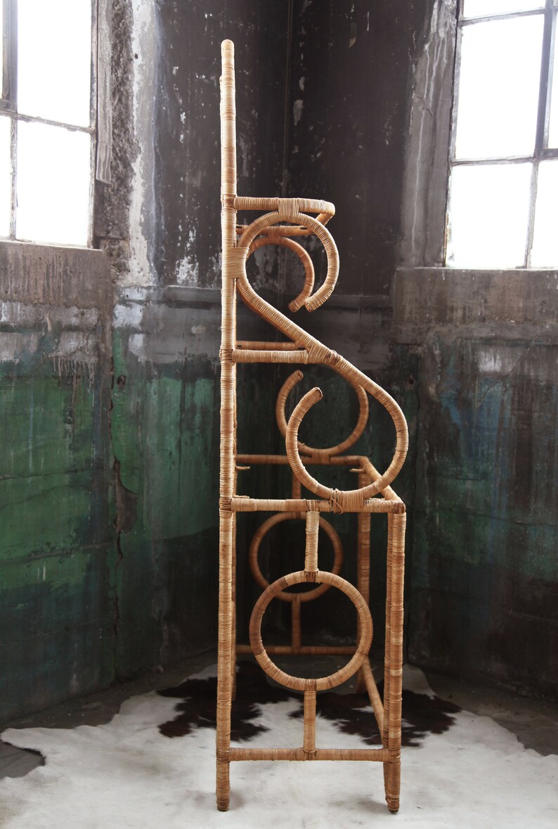 May include: A tall, natural woven rattan shelf unit with a unique, curved design. The shelf has four levels and is made of natural, light brown rattan.