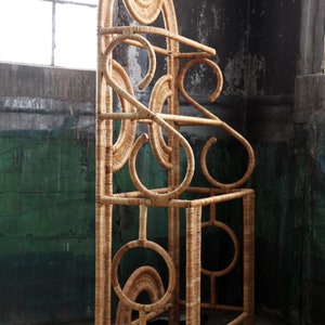 May include: A tall, free-standing, woven wicker coat rack with a geometric design. The rack has a rounded top and multiple shelves.