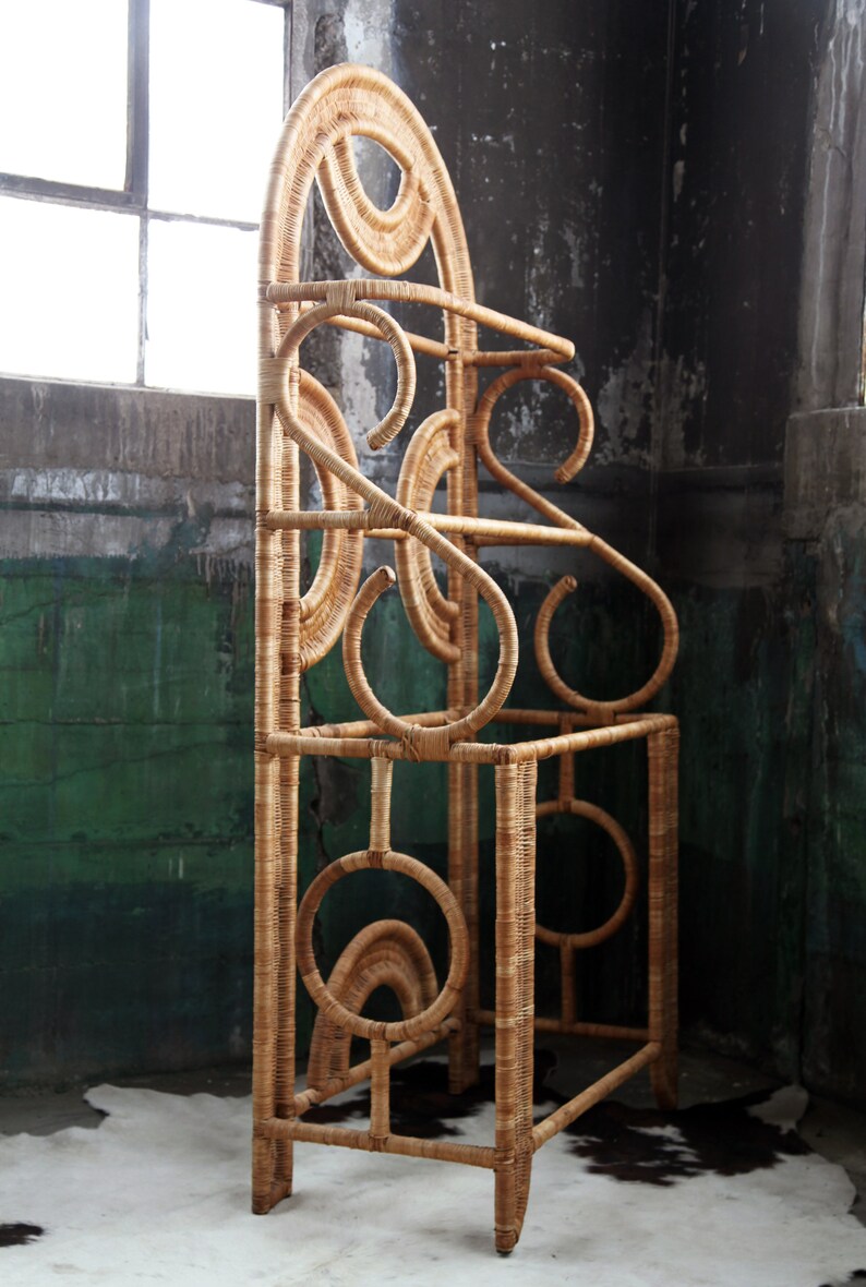 May include: A tall, free-standing, woven wicker coat rack with a geometric design. The rack has a rounded top and multiple shelves.