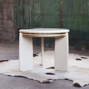 May include: White round side table with gold trim around the top edge. The table has four legs and a single support post in the center.