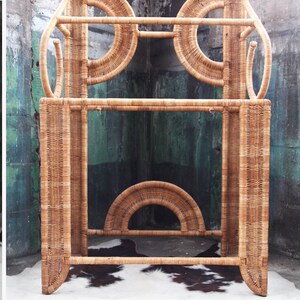 May include: A tall, natural wicker shelf unit with a geometric design. The shelf has three levels and is made of woven rattan.