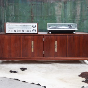 May include: A vintage wooden cabinet with four doors and brass handles. A silver stereo receiver and a turntable are sitting on top of the cabinet.