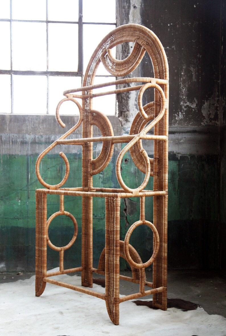 May include: A tall, free-standing, woven wicker shelf unit with a geometric design. The shelf has three tiers and is made of natural brown wicker.
