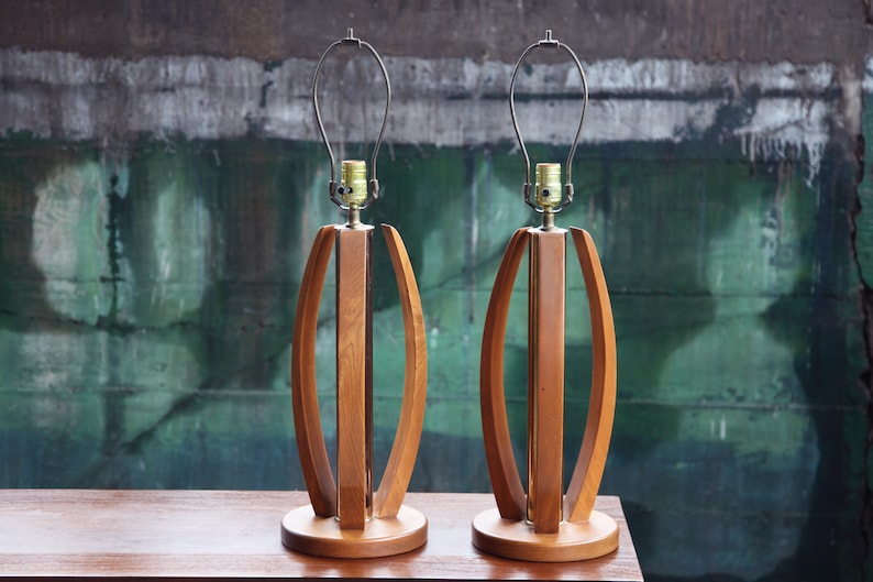 Pode incluir: Um par de candeeiros de mesa de estilo moderno de meados do s&eacute;culo com bases de madeira e abajures de metal. Os candeeiros t&ecirc;m um acabamento de madeira natural quente e um design simples e elegante.