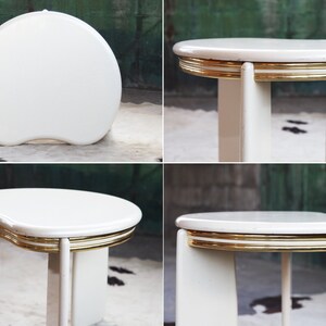 May include: White oval-shaped side table with a gold trim around the edge of the top. The table has a unique, modern design with a curved top and four legs.