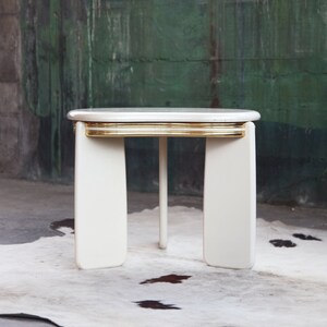 May include: White oval side table with a gold trim around the top edge. The table has four legs and is sitting on a white rug.