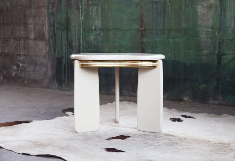 May include: White oval side table with a gold trim around the top edge. The table has four legs and is sitting on a white rug.