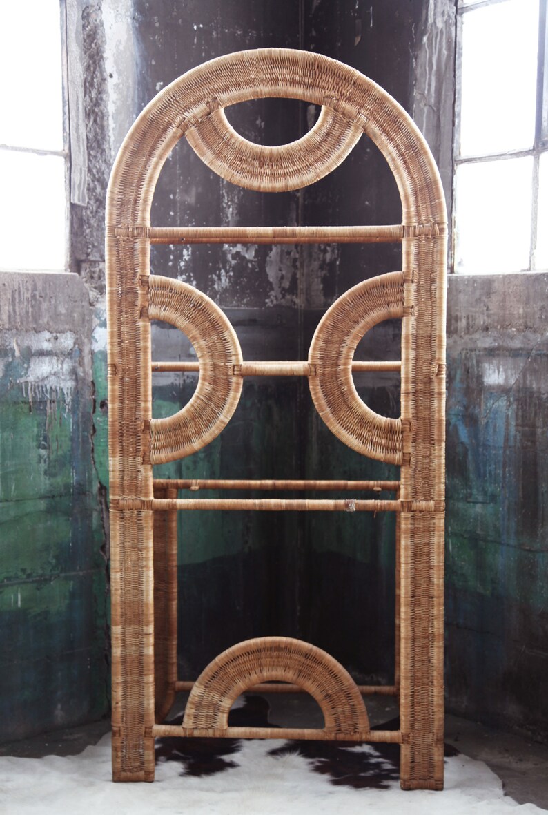 May include: A tall, arched, woven wicker shelf unit with a geometric design. The shelf has three levels and is made of natural, light brown wicker.