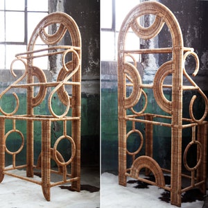 May include: A tall, woven wicker shelf unit with a rounded arch top and multiple circular and semi-circular cutouts. The shelf has three tiers and is made of natural brown wicker.