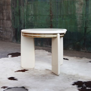 May include: White round nesting table with gold trim. The table is made of wood and has a modern design.