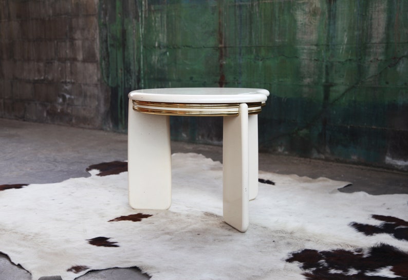 May include: White round nesting table with gold trim. The table is made of wood and has a modern design.