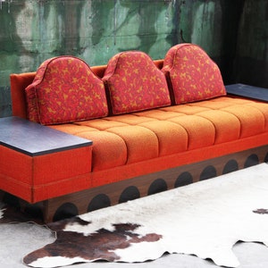 May include: A vintage orange and brown sofa with three cushions and two side tables. The sofa has a unique design with a black and brown base.
