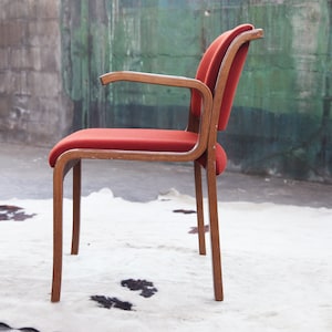 May include: A red upholstered chair with wooden arms and legs. The chair is sitting on a white cowhide rug.