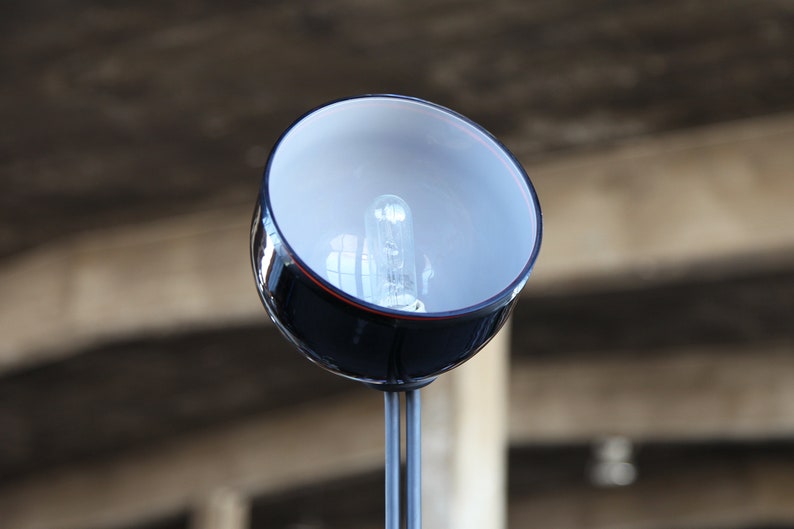 Może przedstawiać: Czarna i srebrna lampa z okrągłym, białym kloszem ze szkła i żar&oacute;wką w środku.
