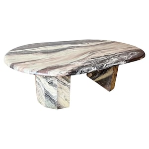 May include: A large oval-shaped coffee table made of marble with a swirling pattern of brown, white, and grey. The table has four legs that are also made of marble.