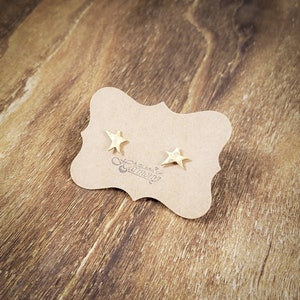 May include: A pair of gold star-shaped stud earrings on a brown card with the text "A Glass of Caution".