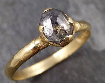 May include: A gold ring with a grey, faceted, rough-cut diamond. The ring band is hammered and has a textured finish.