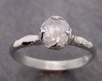 Könnte beinhalten: Ein silberner Ring mit einem weißen, runden, facettierten Edelstein, der in einer Krappenfassung sitzt.
