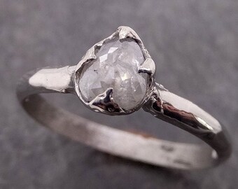 May include: A silver ring with a clear, faceted, rough-cut diamond set in a delicate, organic-shaped setting.