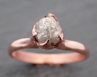 May include: A rose gold ring with a raw, white diamond set in a delicate, claw-like setting.