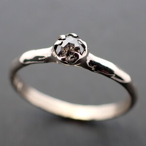 Puede incluir: Un anillo de plata con un diamante negro engastado en una banda texturizada.