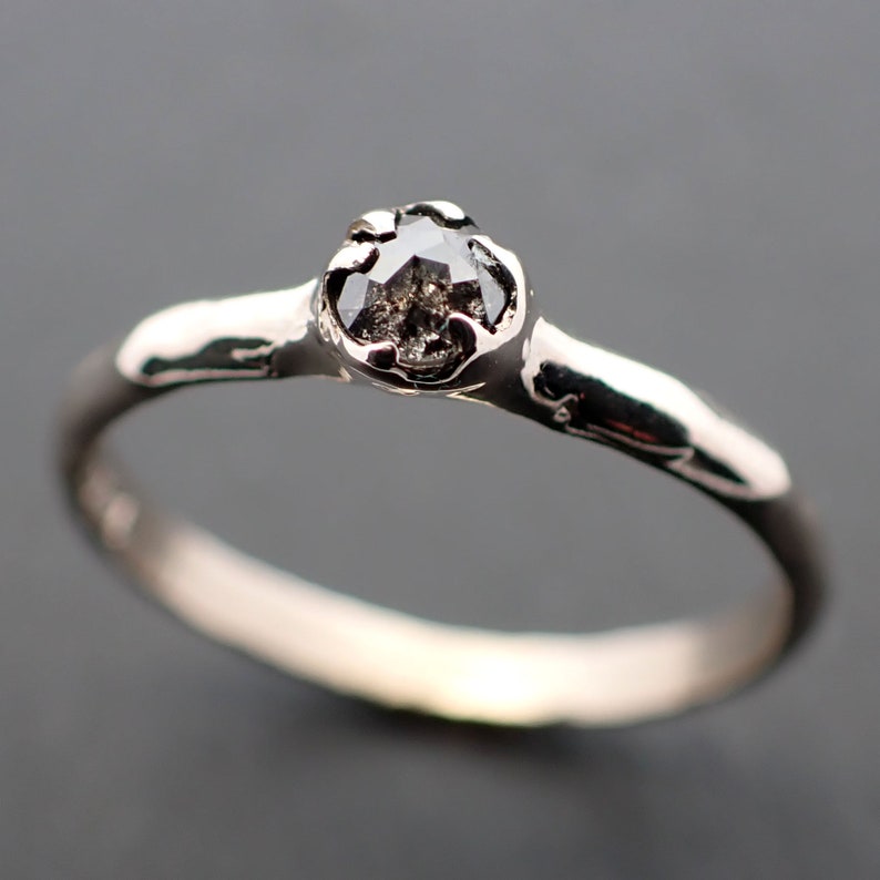 Puede incluir: Un anillo de plata con un diamante negro engastado en una banda texturizada.