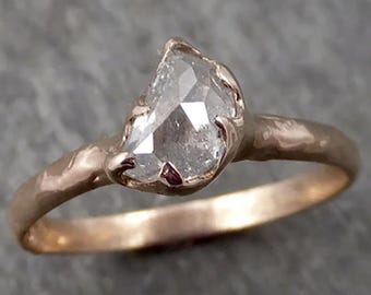 Può includere: Un anello con fascia in oro rosa dalla finitura martellata e testurizzata. La pietra centrale è un diamante traslucido di forma irregolare e semicircolare, fissato da quattro piccole griffe che lo ancorano alla fascia metallica.