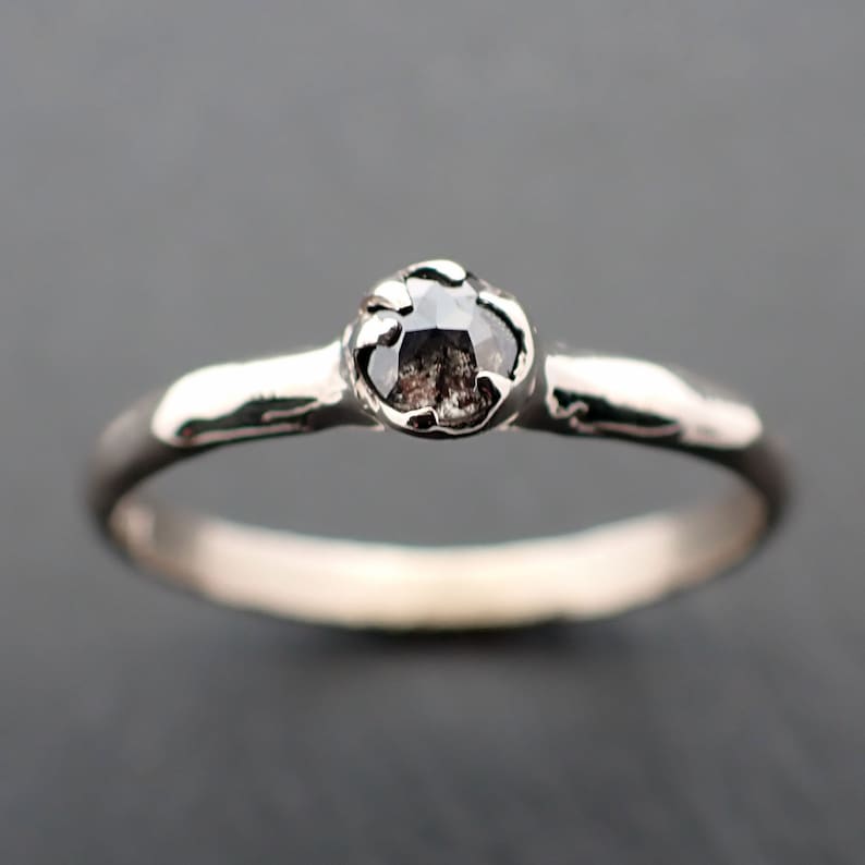 Puede incluir: Un anillo de plata con un diamante negro engastado en una banda texturizada.