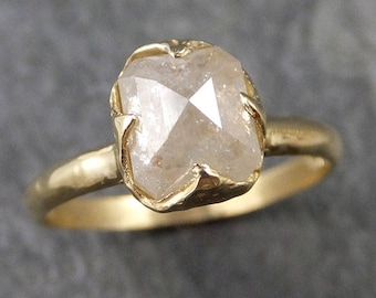 Op de afbeelding: Een gouden ring met een grote, heldere, gefacetteerde, ruwe diamant gezet in een gouden bezel setting.