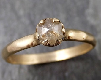 Puede incluir: Un anillo de oro con un diamante redondo, facetado, marrón claro engastado en una banda simple y texturizada.
