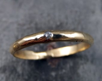 Può includere: Un semplice anello a fascia d'oro con un piccolo diamante grigio incastonato al centro.