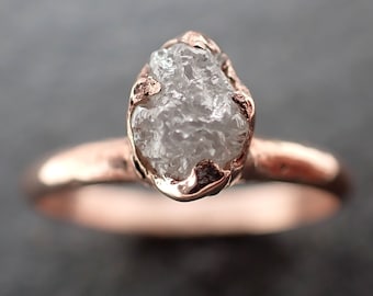 May include: A rose gold ring with a rough, white diamond set in a simple band.