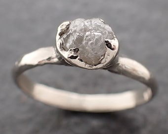 May include: A silver ring with a rough, natural diamond set in a textured band.