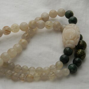 May include: A double-strand necklace with white and gold beads and a green jade pendant with a carved design. The pendant is attached to a green jade bead.