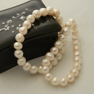 May include: A strand of white pearls in a black box with a floral design. The pearls are round and smooth.