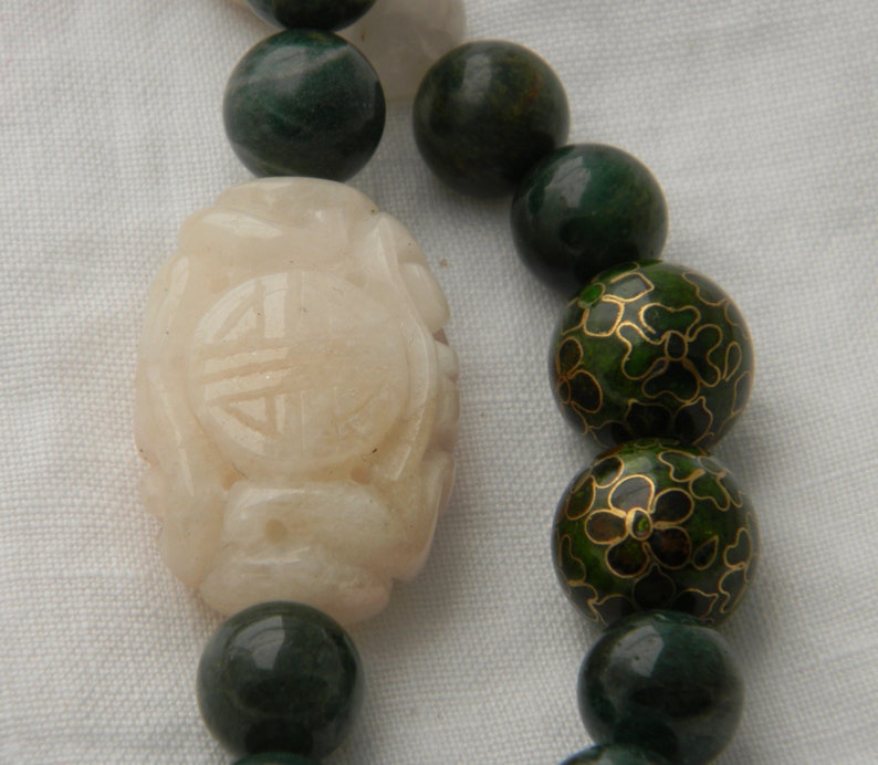 May include: A white jade bead with a carved design, surrounded by green jade and green enamel beads with gold floral patterns.