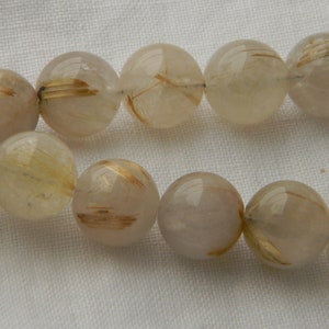 May include: A strand of clear quartz beads with gold inclusions. The beads are round and have a smooth, polished finish.