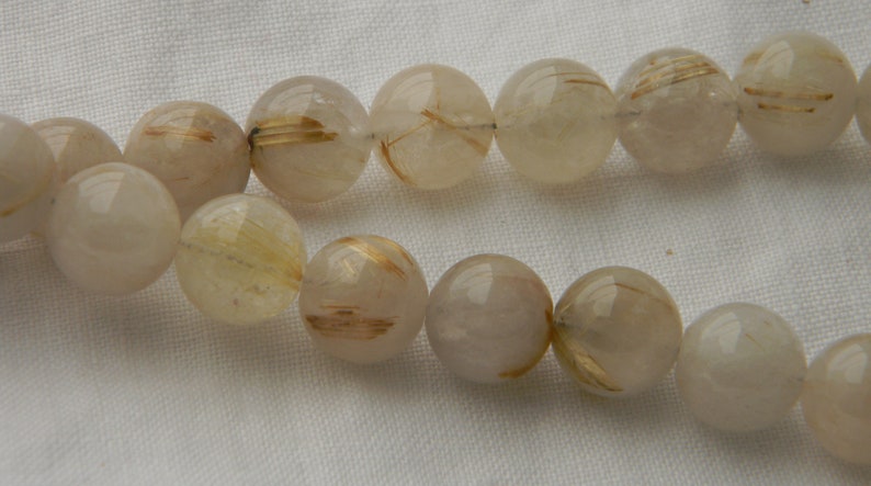 May include: A strand of clear quartz beads with gold inclusions. The beads are round and have a smooth, polished finish.