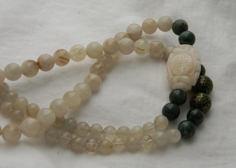 May include: A double-strand necklace with white and gold beads and a green jade pendant with a carved design. The pendant is attached to a green jade bead.