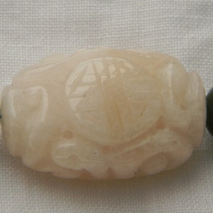 May include: A bracelet made of dark green and light pink beads. The pink bead is carved with a detailed design.
