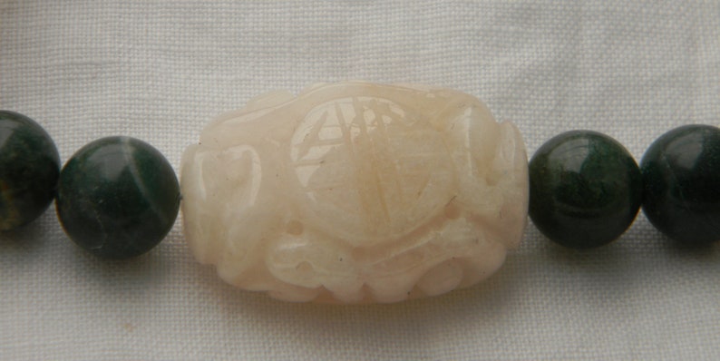 May include: A bracelet made of dark green and light pink beads. The pink bead is carved with a detailed design.