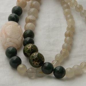 May include: A multi-strand necklace with green, white, and gold beads. The necklace features a large, carved, pink bead.