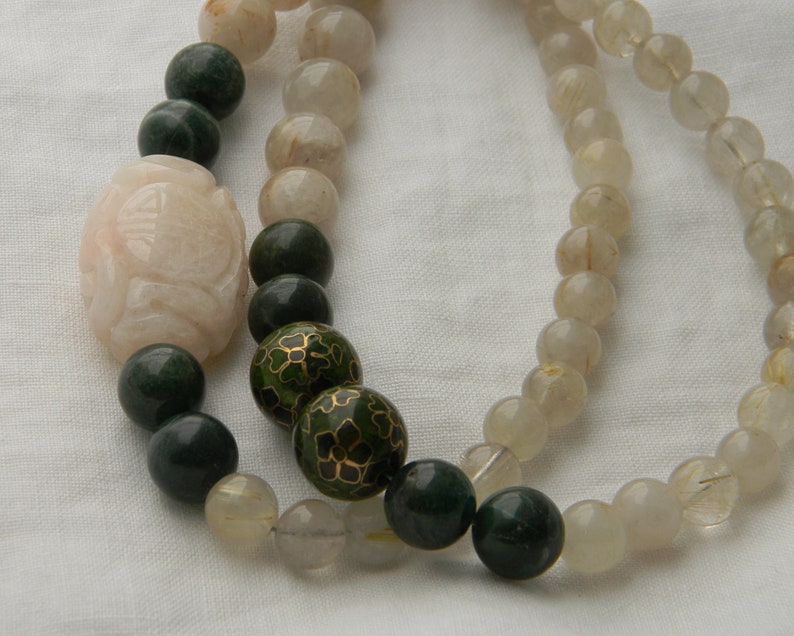 May include: A multi-strand necklace with green, white, and gold beads. The necklace features a large, carved, pink bead.