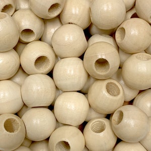 May include: A close-up of a pile of natural wood beads with a hole in the center of each bead. The beads are smooth and have a light brown color.