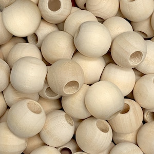 May include: A close-up of a pile of natural wood beads with a hole in the center of each bead. The beads are smooth and round, and they are all the same size.